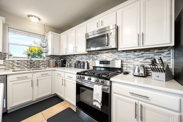 kitchen with stainless steel appliances, light tile patterned floors, sink, white cabinetry, and backsplash