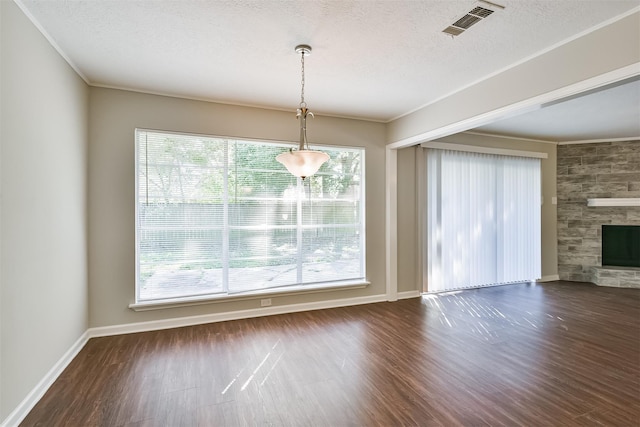 unfurnished dining area with a tiled fireplace, plenty of natural light, crown molding, and dark wood-type flooring