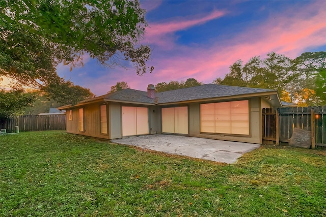 back house at dusk with a patio area and a yard