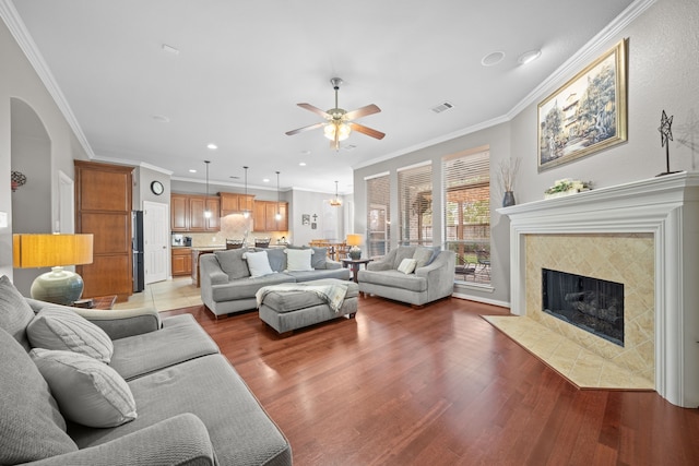 living room featuring ceiling fan, a tile fireplace, crown molding, and wood-type flooring