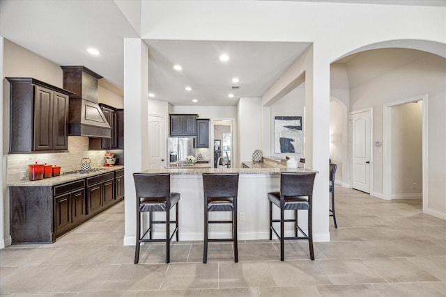 kitchen featuring light stone countertops, decorative backsplash, appliances with stainless steel finishes, and a kitchen breakfast bar