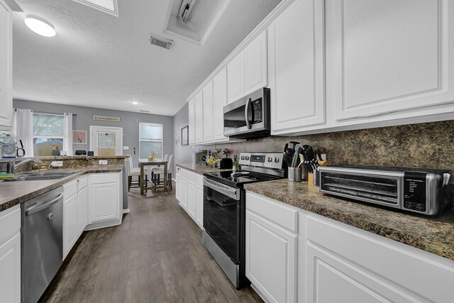 kitchen with stainless steel appliances, dark hardwood / wood-style flooring, white cabinets, dark stone countertops, and sink