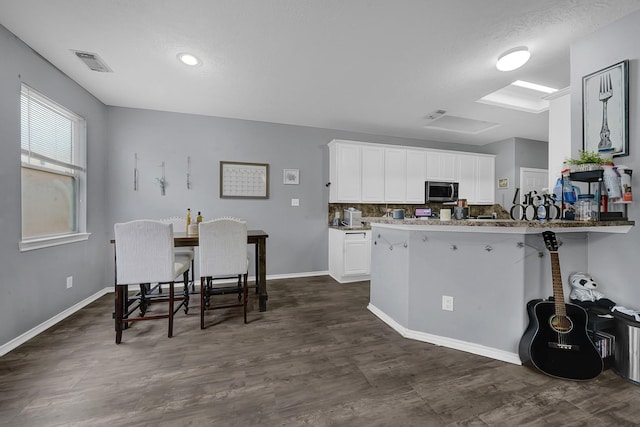 kitchen featuring kitchen peninsula, a kitchen bar, white cabinetry, stone countertops, and backsplash