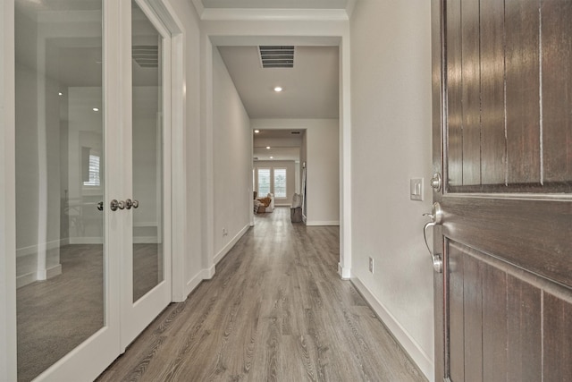 corridor with french doors, light wood-type flooring, and crown molding