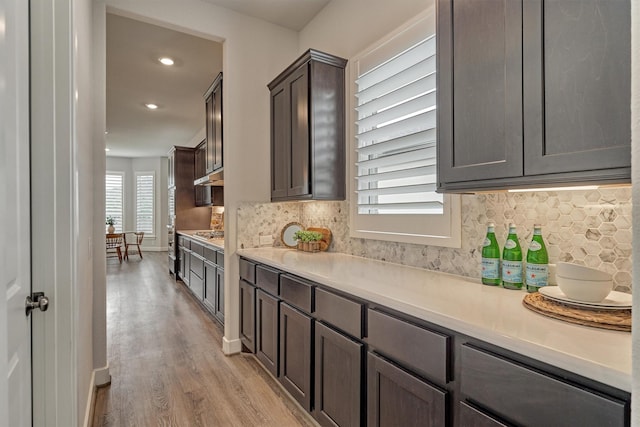 kitchen with dark brown cabinetry, stainless steel gas stovetop, light hardwood / wood-style floors, and backsplash