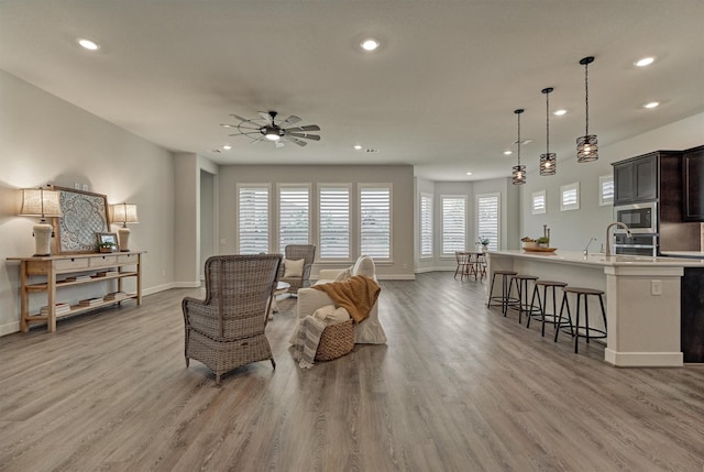 living room featuring ceiling fan, sink, and light wood-type flooring