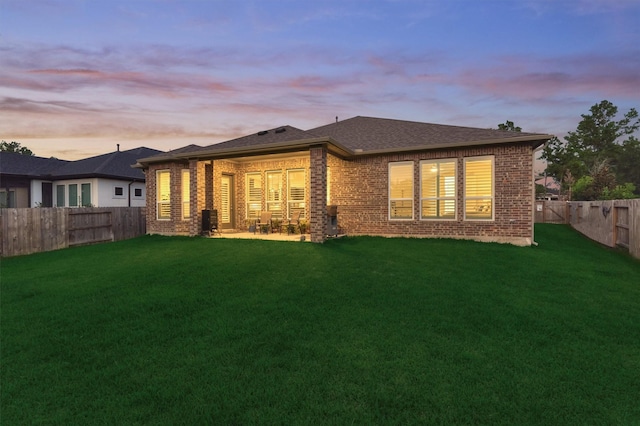 back house at dusk featuring a lawn