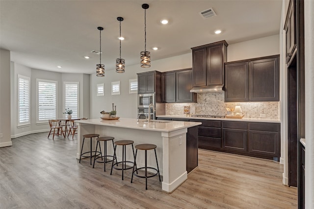 kitchen featuring sink, hanging light fixtures, appliances with stainless steel finishes, a kitchen island with sink, and light hardwood / wood-style floors