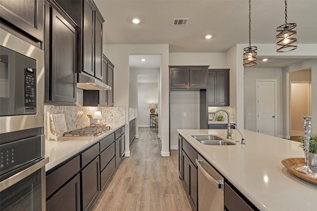 kitchen featuring dark brown cabinetry, sink, appliances with stainless steel finishes, pendant lighting, and decorative backsplash