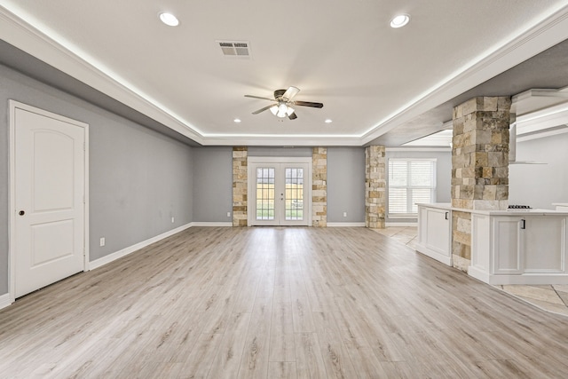 unfurnished living room with decorative columns, french doors, a raised ceiling, ceiling fan, and light hardwood / wood-style floors