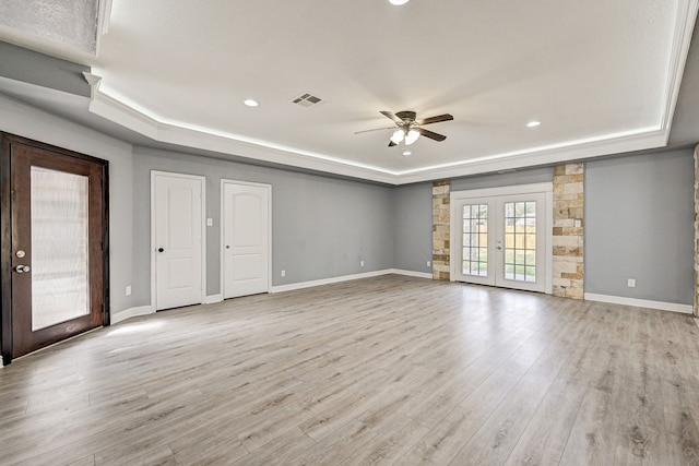 empty room featuring ceiling fan, light hardwood / wood-style flooring, french doors, and a tray ceiling