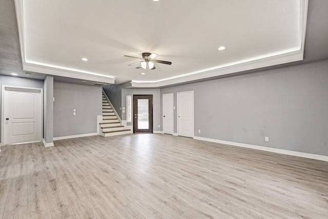 unfurnished living room featuring a raised ceiling, ceiling fan, and light hardwood / wood-style flooring