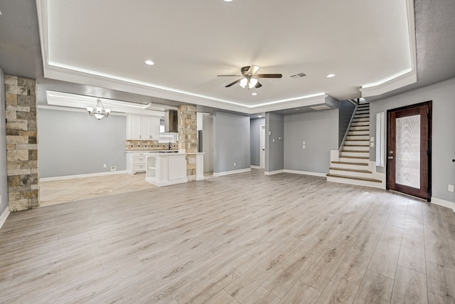 unfurnished living room featuring light wood-type flooring, ceiling fan with notable chandelier, and a tray ceiling