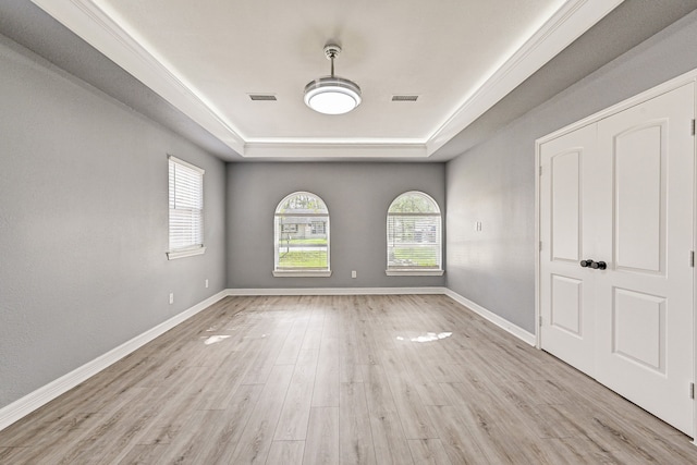 empty room with light wood-type flooring and a tray ceiling