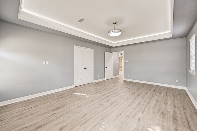 spare room with a tray ceiling and light hardwood / wood-style floors