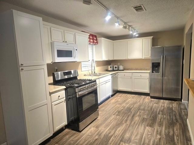 kitchen featuring appliances with stainless steel finishes, light hardwood / wood-style floors, a textured ceiling, white cabinetry, and sink