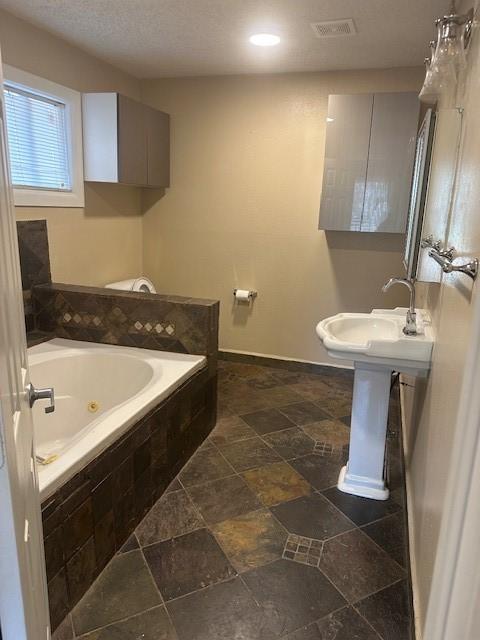 bathroom featuring sink, a textured ceiling, and tiled bath