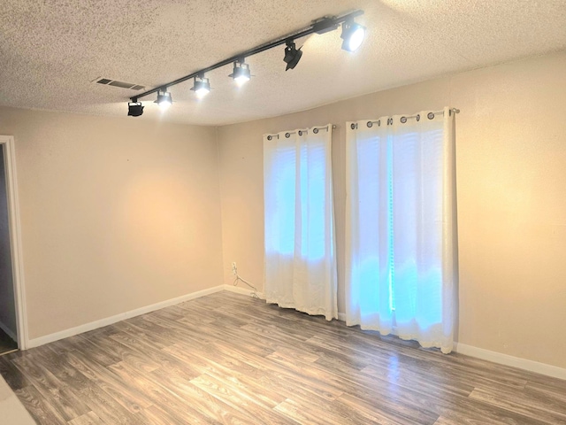 empty room with a textured ceiling, rail lighting, and hardwood / wood-style floors