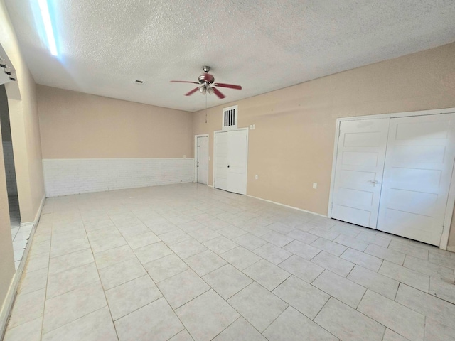 unfurnished bedroom with ceiling fan, a textured ceiling, brick wall, and light tile patterned floors