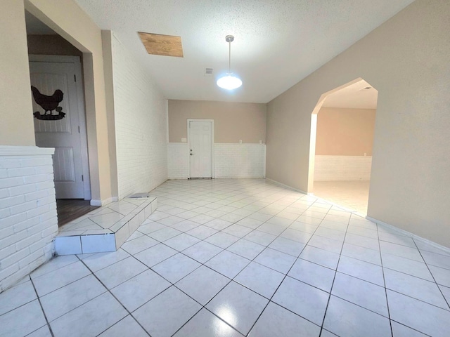 empty room with a textured ceiling, brick wall, and light tile patterned floors