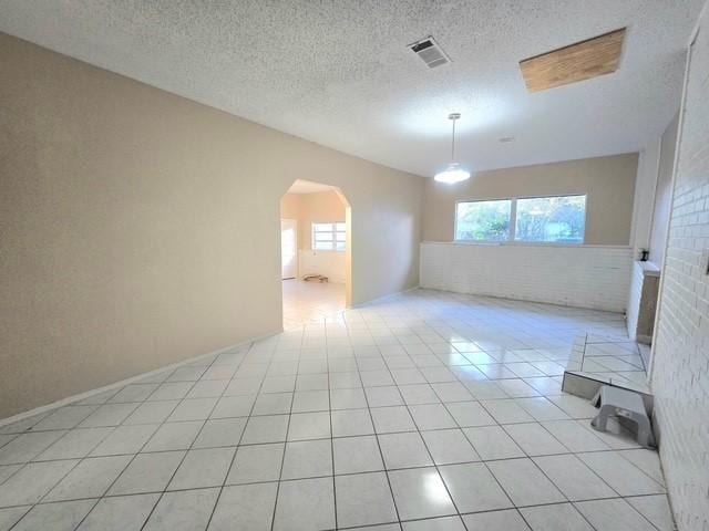 tiled empty room with a textured ceiling and brick wall