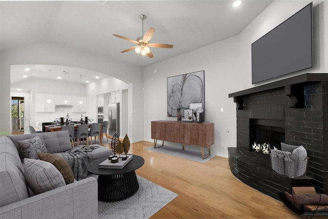 living room with ceiling fan, light wood-type flooring, lofted ceiling, and a fireplace