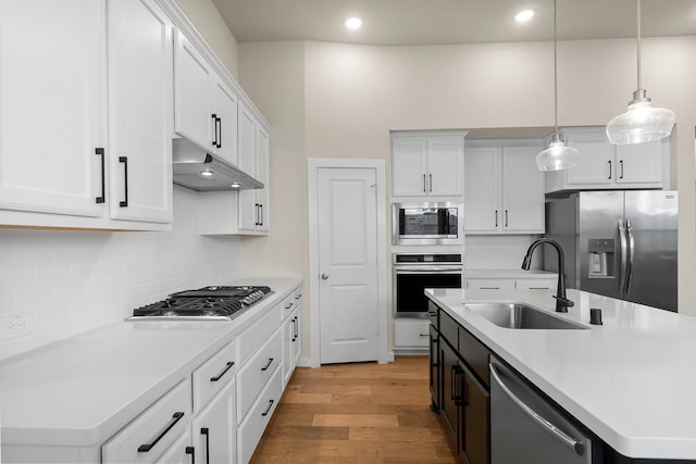 kitchen featuring hanging light fixtures, stainless steel appliances, a center island with sink, white cabinets, and sink