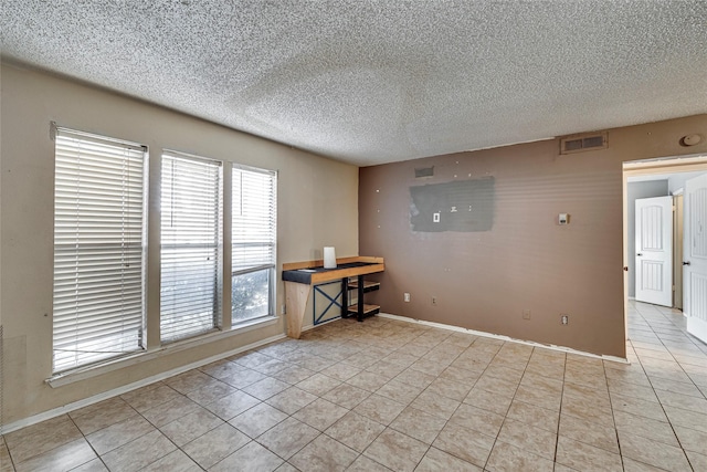 tiled empty room featuring a textured ceiling and plenty of natural light