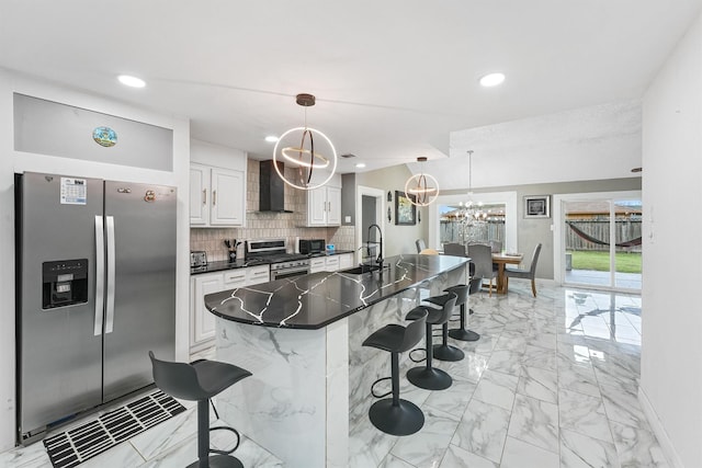 kitchen featuring stainless steel appliances, a kitchen breakfast bar, wall chimney range hood, pendant lighting, and white cabinets