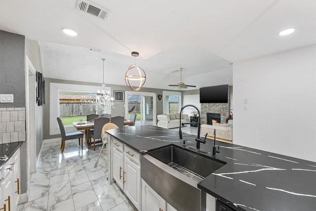 kitchen with white cabinetry, a stone fireplace, ceiling fan, pendant lighting, and sink