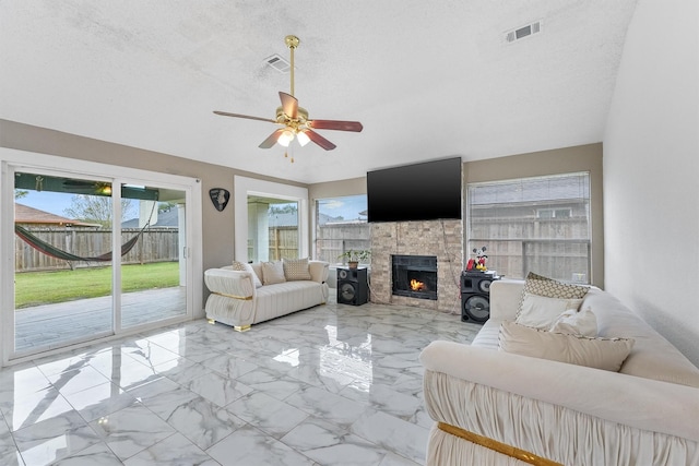 living room with ceiling fan, a textured ceiling, a healthy amount of sunlight, and a fireplace