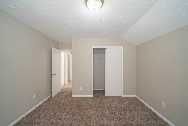 unfurnished bedroom with a textured ceiling, a closet, vaulted ceiling, and carpet floors