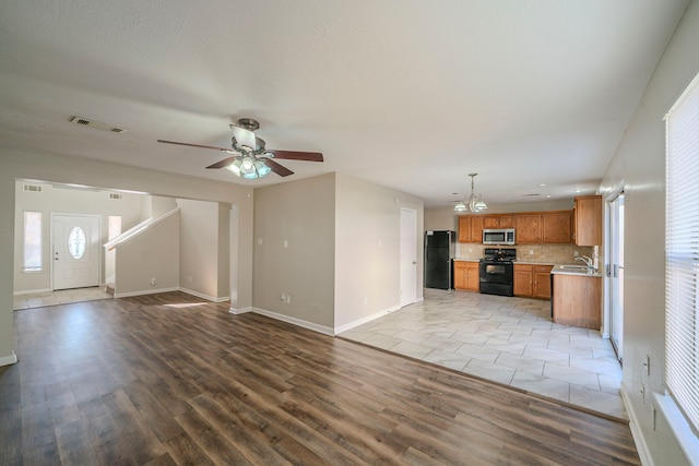 unfurnished living room featuring ceiling fan with notable chandelier, sink, and light hardwood / wood-style flooring