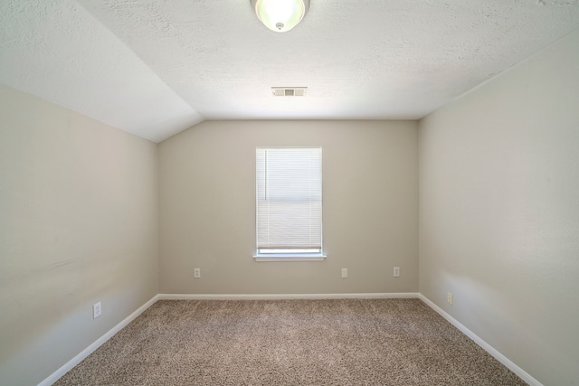 carpeted empty room featuring vaulted ceiling and a textured ceiling