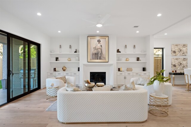 living room featuring ceiling fan, built in shelves, and light hardwood / wood-style floors