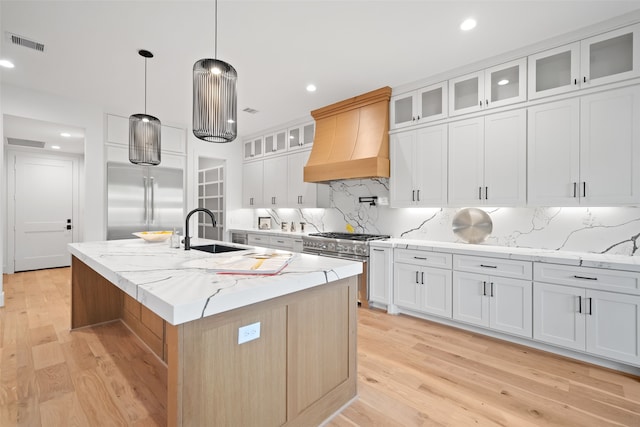 kitchen featuring white cabinets, sink, hanging light fixtures, premium range hood, and a kitchen island with sink