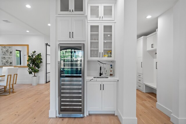 bar featuring light wood-type flooring, white cabinetry, and beverage cooler