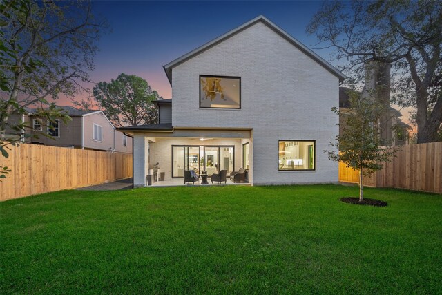 back house at dusk featuring a yard and a patio