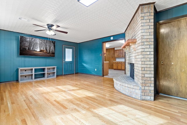 unfurnished living room featuring ceiling fan, light wood-type flooring, and a brick fireplace