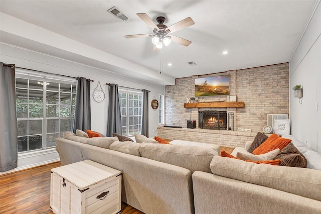 living room with a brick fireplace, brick wall, ceiling fan, and wood-type flooring