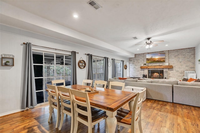 dining area featuring a brick fireplace, ceiling fan, and light hardwood / wood-style flooring