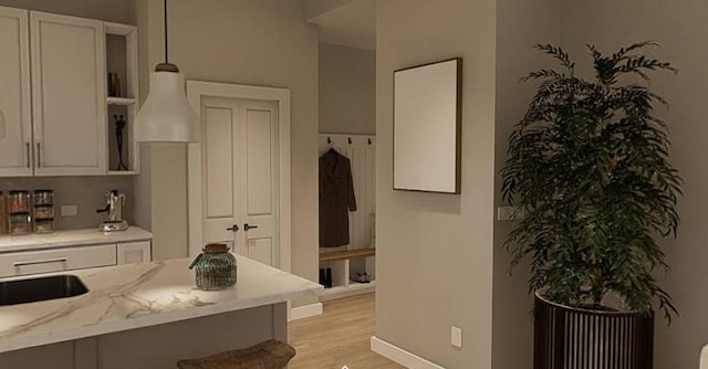 kitchen featuring light stone counters, white cabinets, light wood-type flooring, and hanging light fixtures