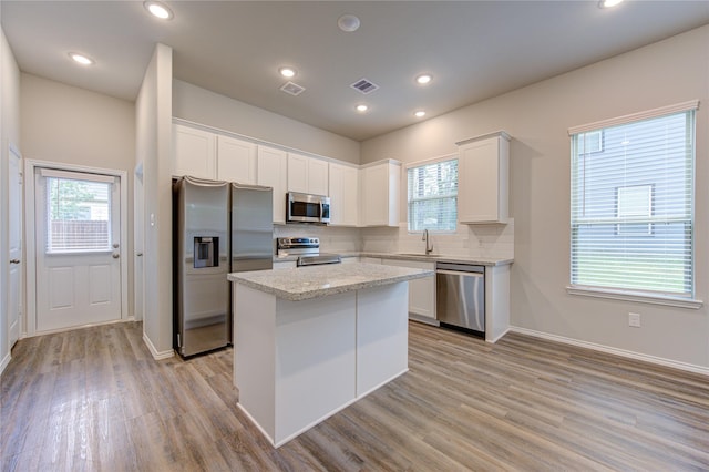 kitchen with light hardwood / wood-style flooring, a center island, white cabinets, appliances with stainless steel finishes, and sink