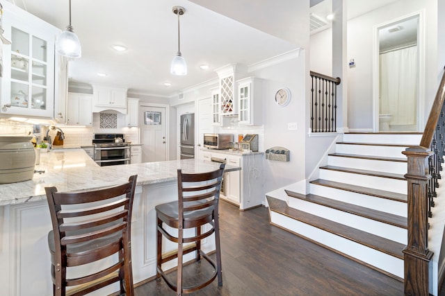 kitchen featuring white cabinetry, stainless steel appliances, backsplash, hanging light fixtures, and a breakfast bar