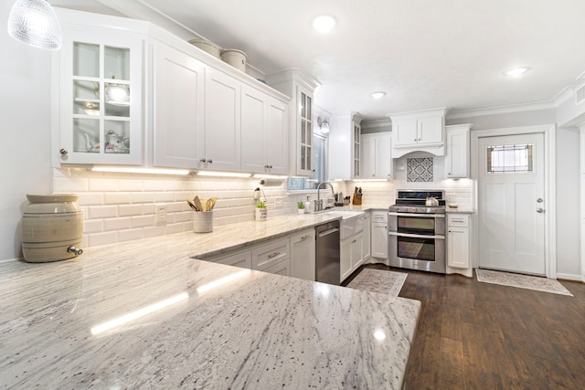 kitchen featuring light stone countertops, white cabinets, appliances with stainless steel finishes, decorative light fixtures, and dark wood-type flooring