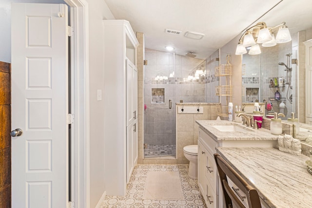 bathroom with a shower with shower door, tile walls, vanity, toilet, and tile patterned floors