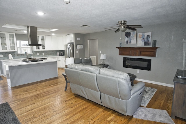 living room with a textured ceiling, ceiling fan, and light hardwood / wood-style flooring