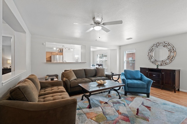 living room with light wood-type flooring, ceiling fan, and a textured ceiling