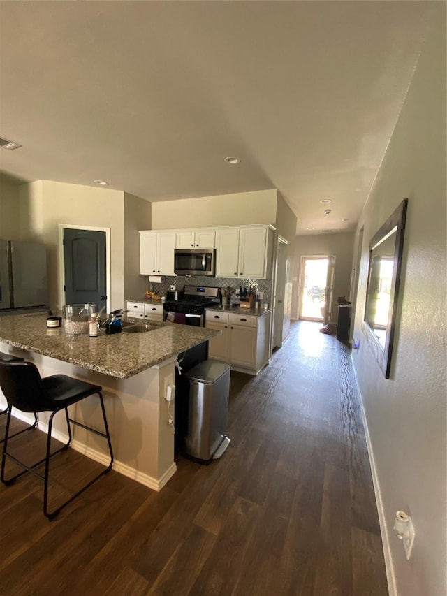 kitchen with a kitchen bar, white cabinets, appliances with stainless steel finishes, and dark wood-type flooring