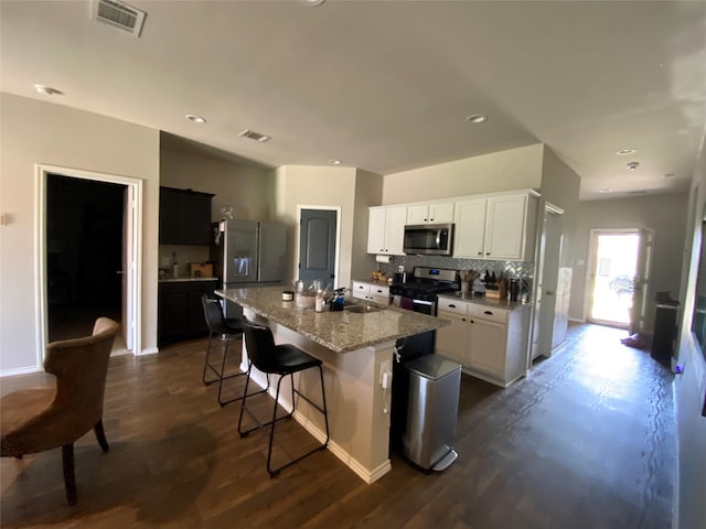 kitchen featuring a kitchen island with sink, a breakfast bar area, stainless steel appliances, white cabinets, and light stone counters